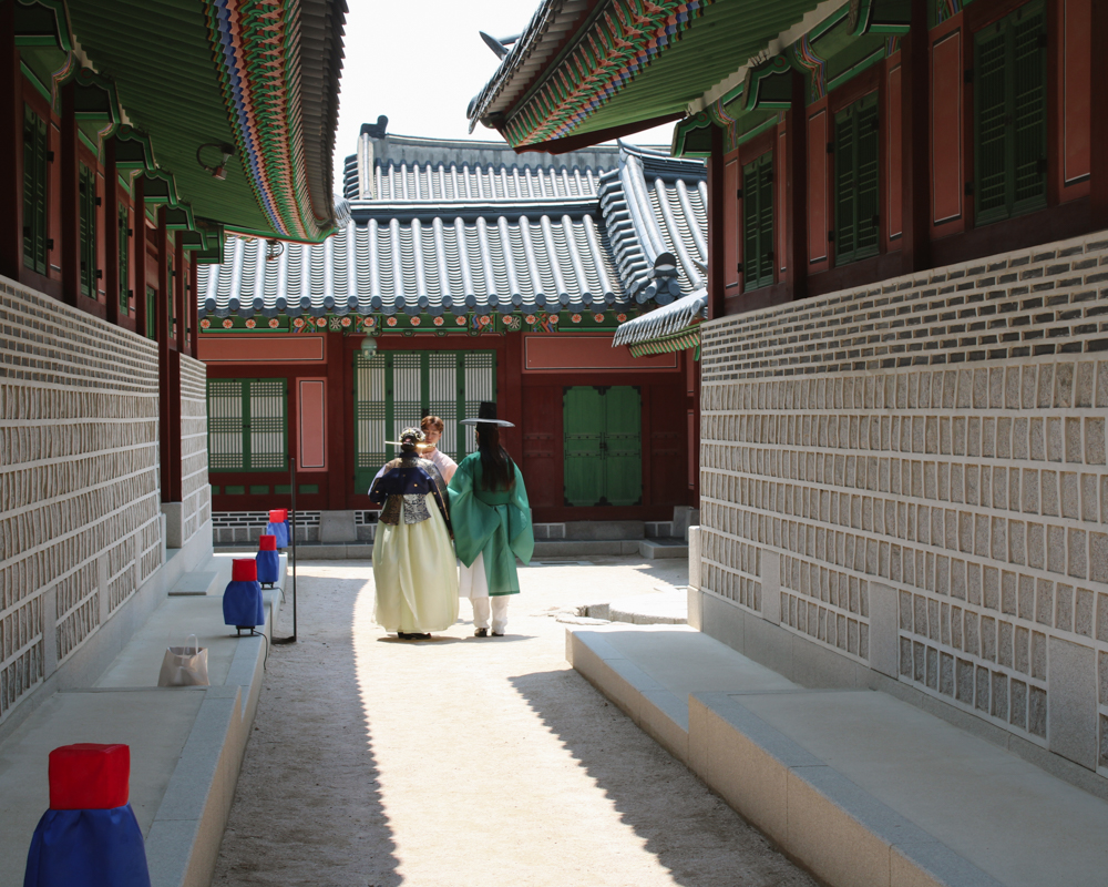 Couple dressed in traditional Korean hanbok strolling through the narrow stone-paved alleys of Bukchon Hanok Village in Seoul, surrounded by historic wooden houses.
