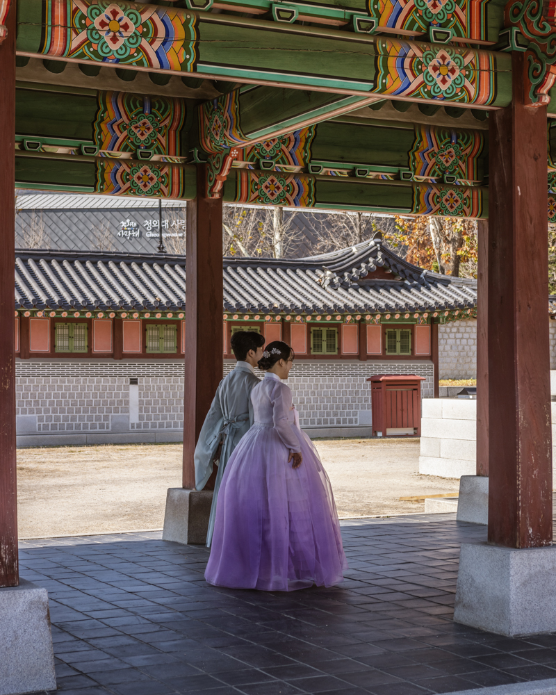 Couple dressed in traditional Korean hanbok strolling through the narrow stone-paved alleys of Hanok Village in Korea, surrounded by historic wooden houses.