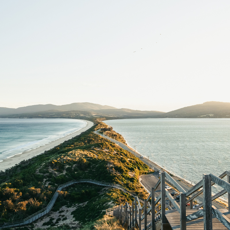 Wooden stairs leading down to the beach at Bruny Island, Tasmania, with dramatic coastal cliffs and turquoise waters in the background