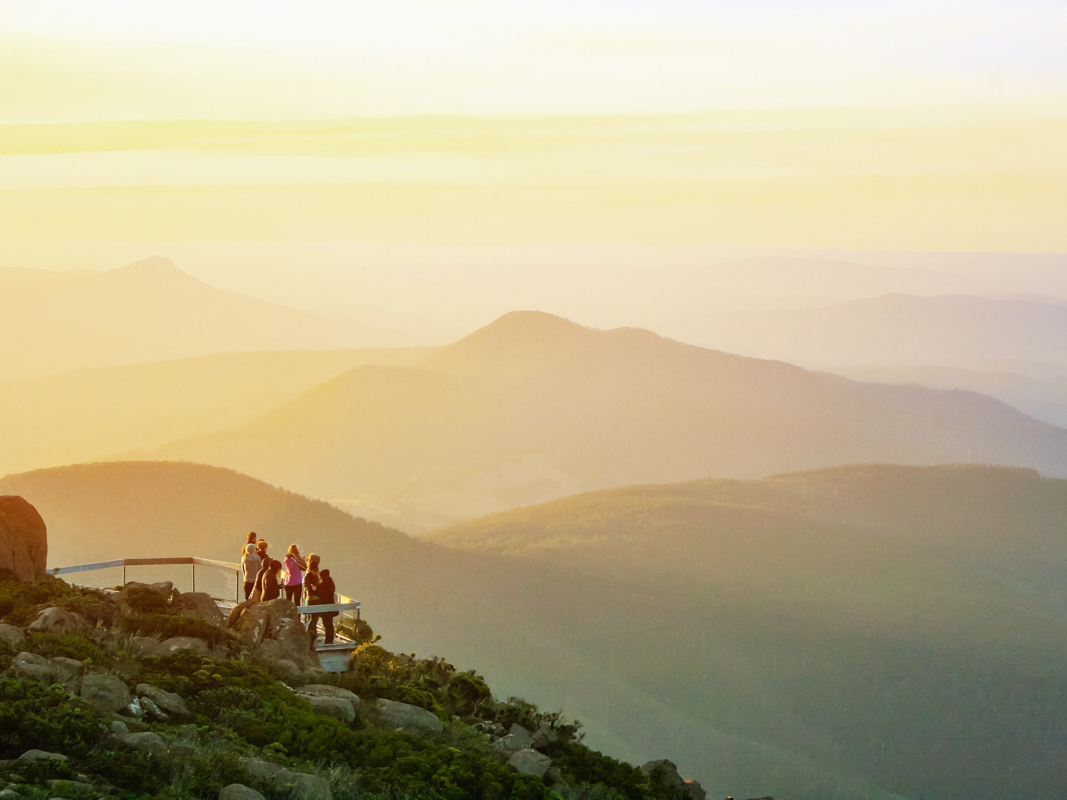 People watching an epic sunset over Hobart from Mount Wellington Lookout, with golden skies and mountain views stretching into the distance