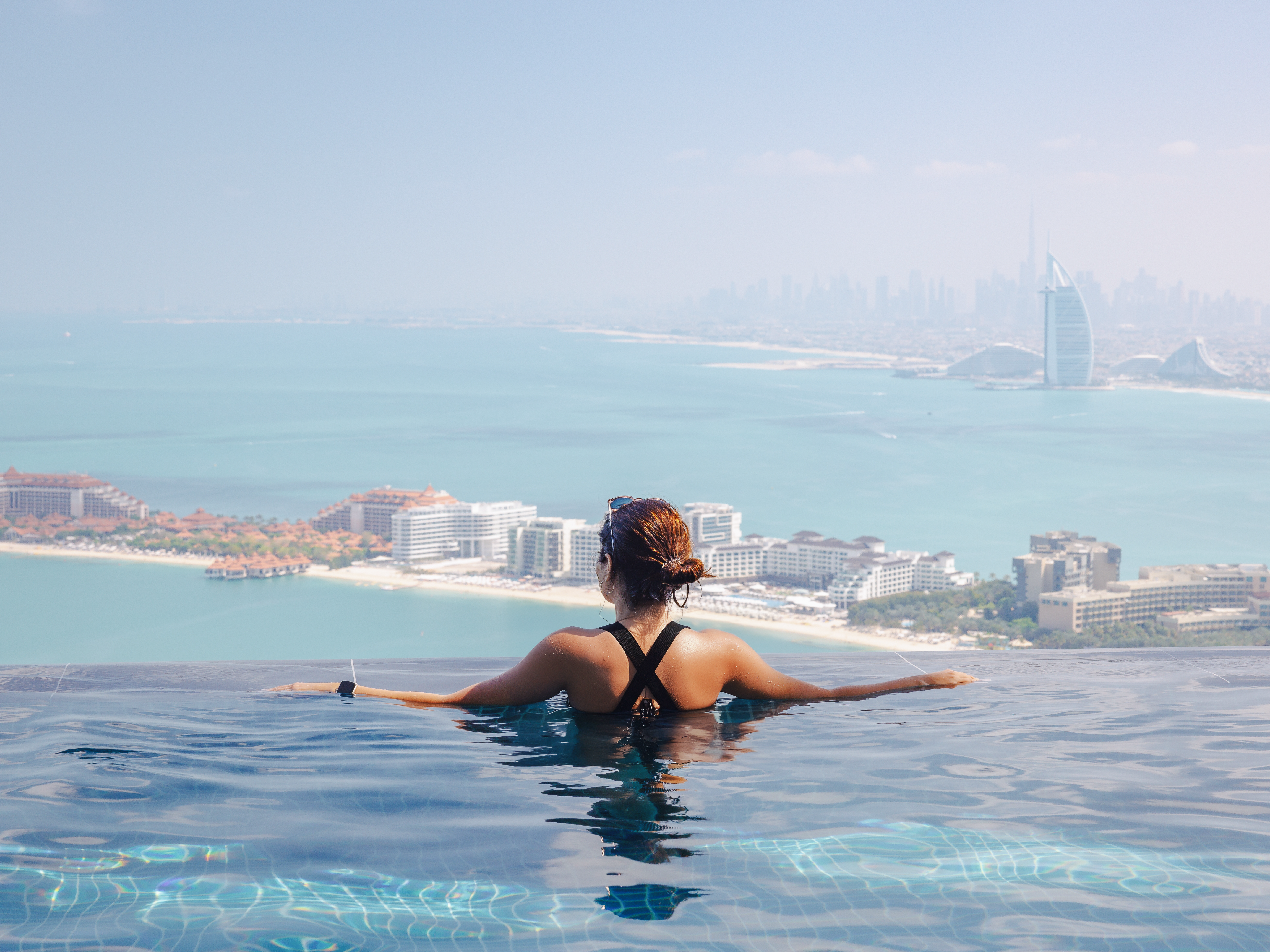 Woman relaxing in an infinity pool overlooking Dubai skyline, reflecting luxury hotels and licensed venues serving alcohol