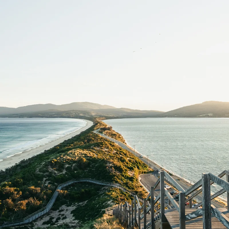 Wooden stairs leading down to the beach at Bruny Island, Tasmania, with dramatic coastal cliffs and turquoise waters in the background