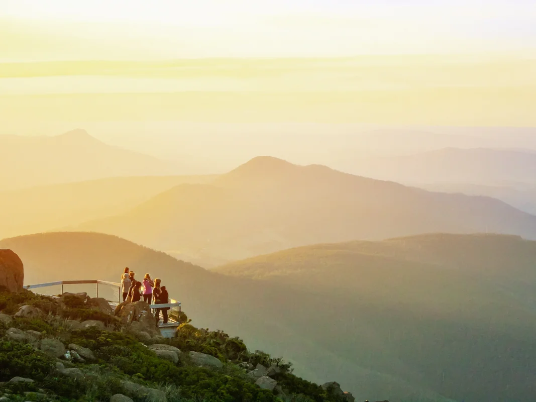 People watching an epic sunset over Hobart from Mount Wellington Lookout, with golden skies and mountain views stretching into the distance