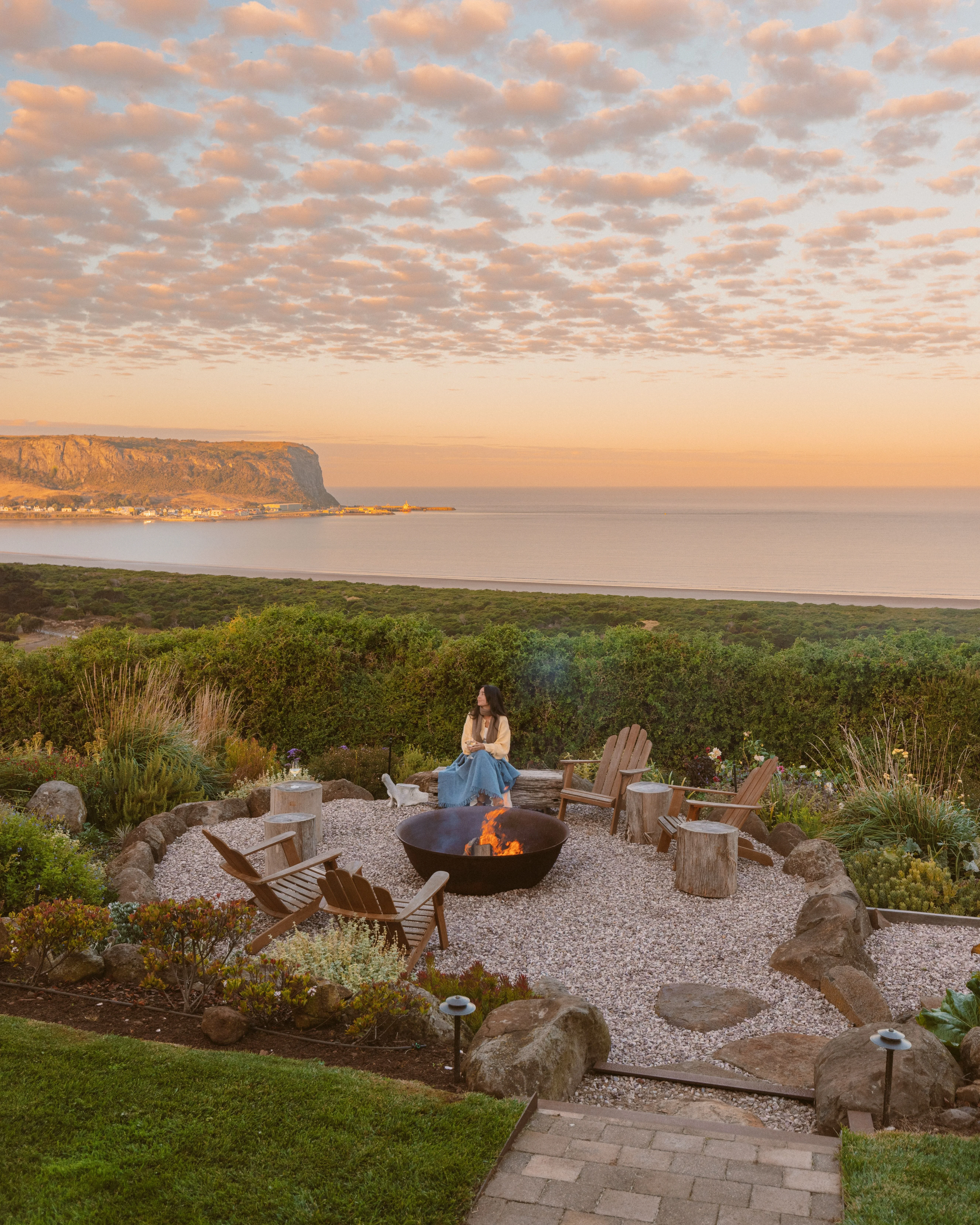 Person relaxing by outdoor fire pit at sunset in Stanley Northern Tasmania with The Nut headland