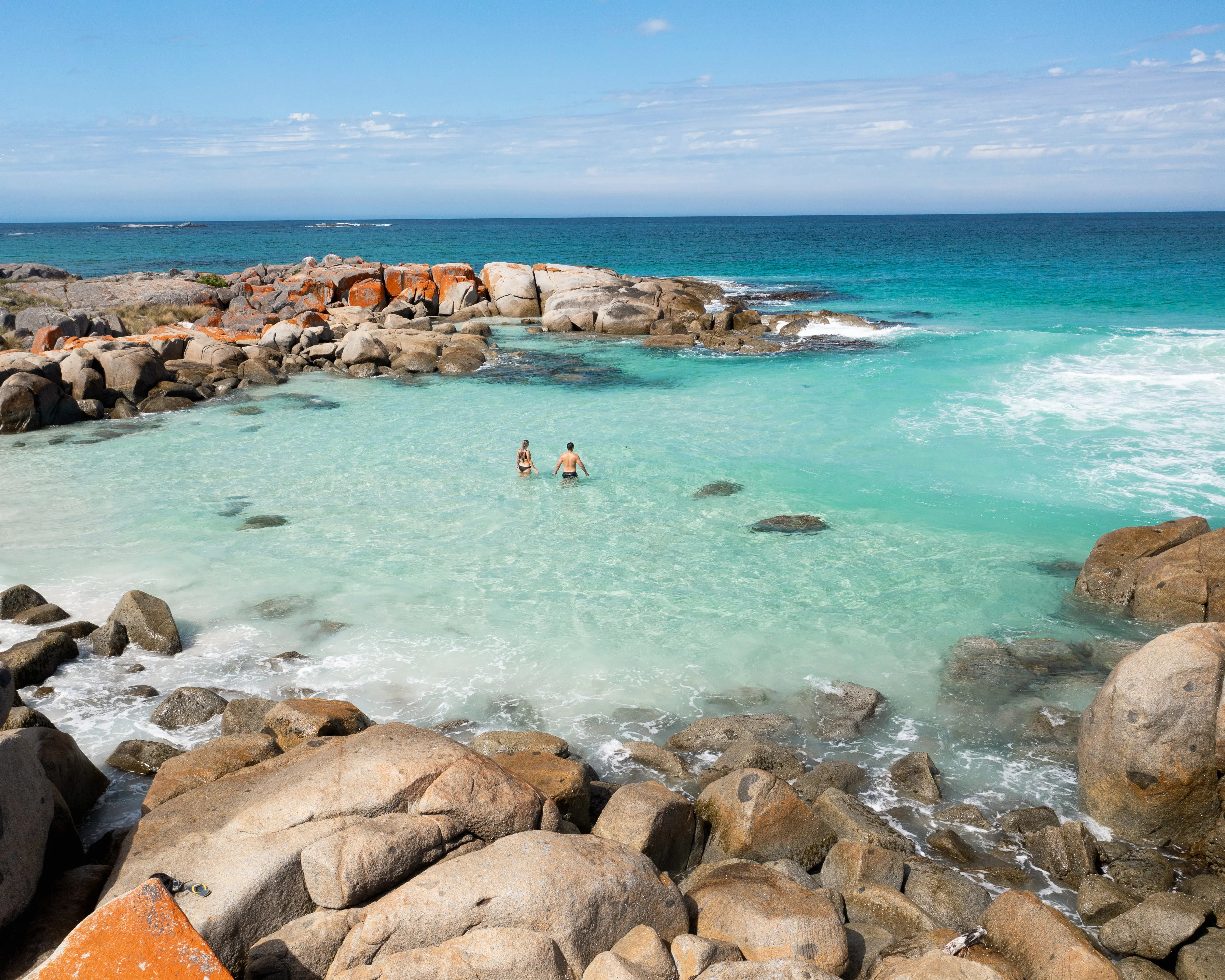 People wading in turquoise waters at Bay of Fires Eastern Tasmania with granite rocks