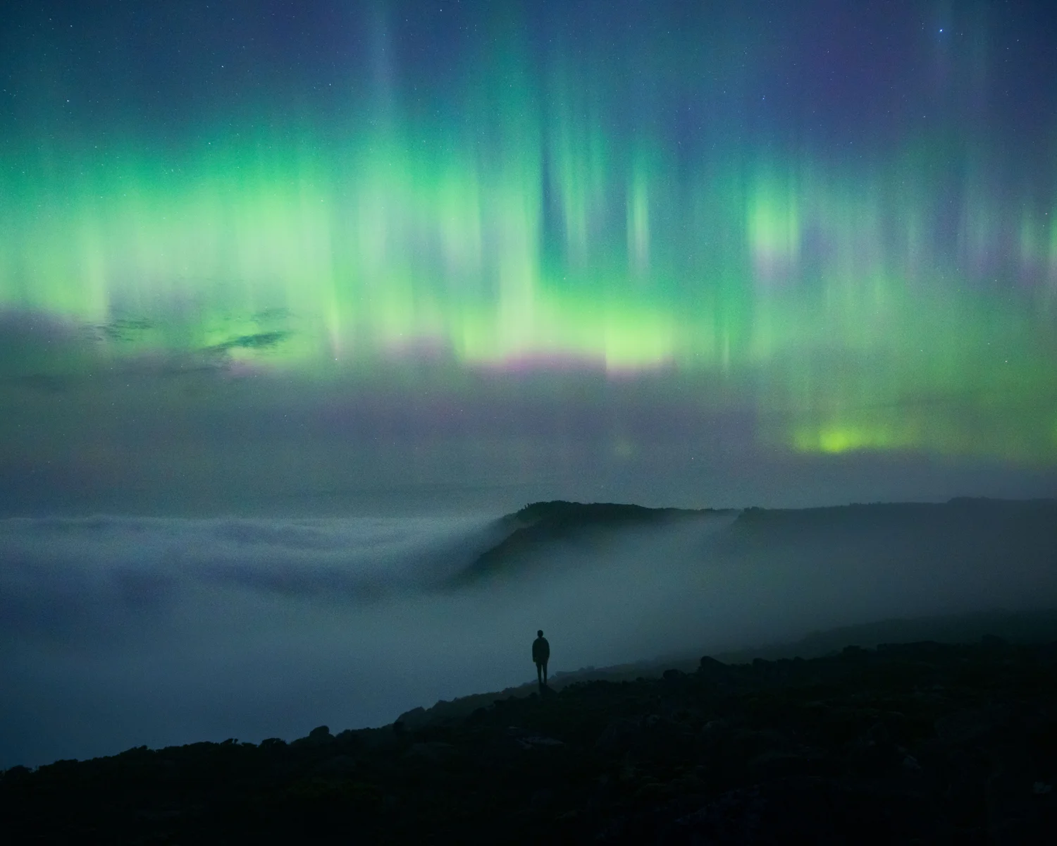 Aurora Australis Southern Lights over rocky summit of Mount Wellington in Hobart Tasmania under vibrant purple and green night sky