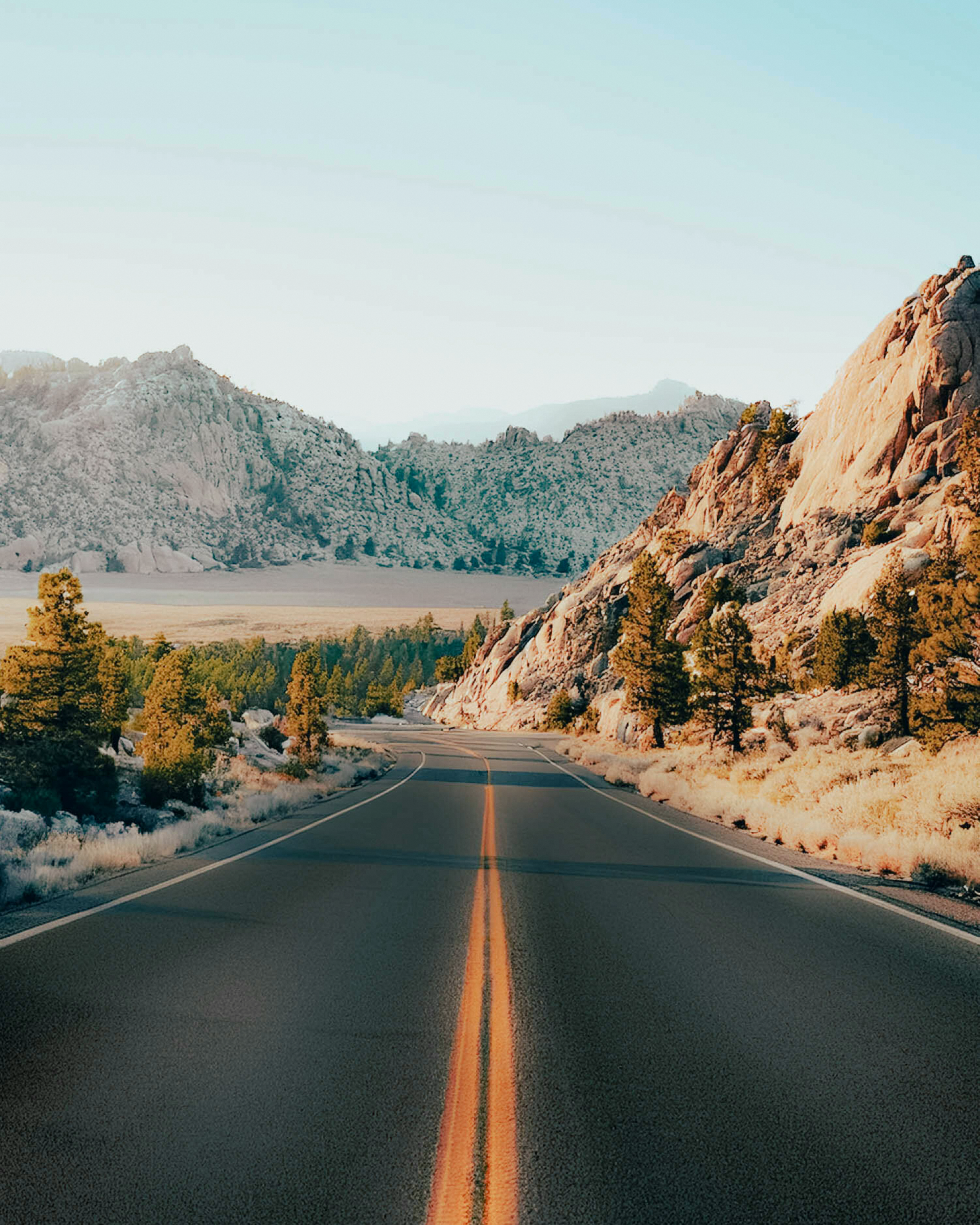 White car driving on a winding road through red rock formations, showing remote travel routes.