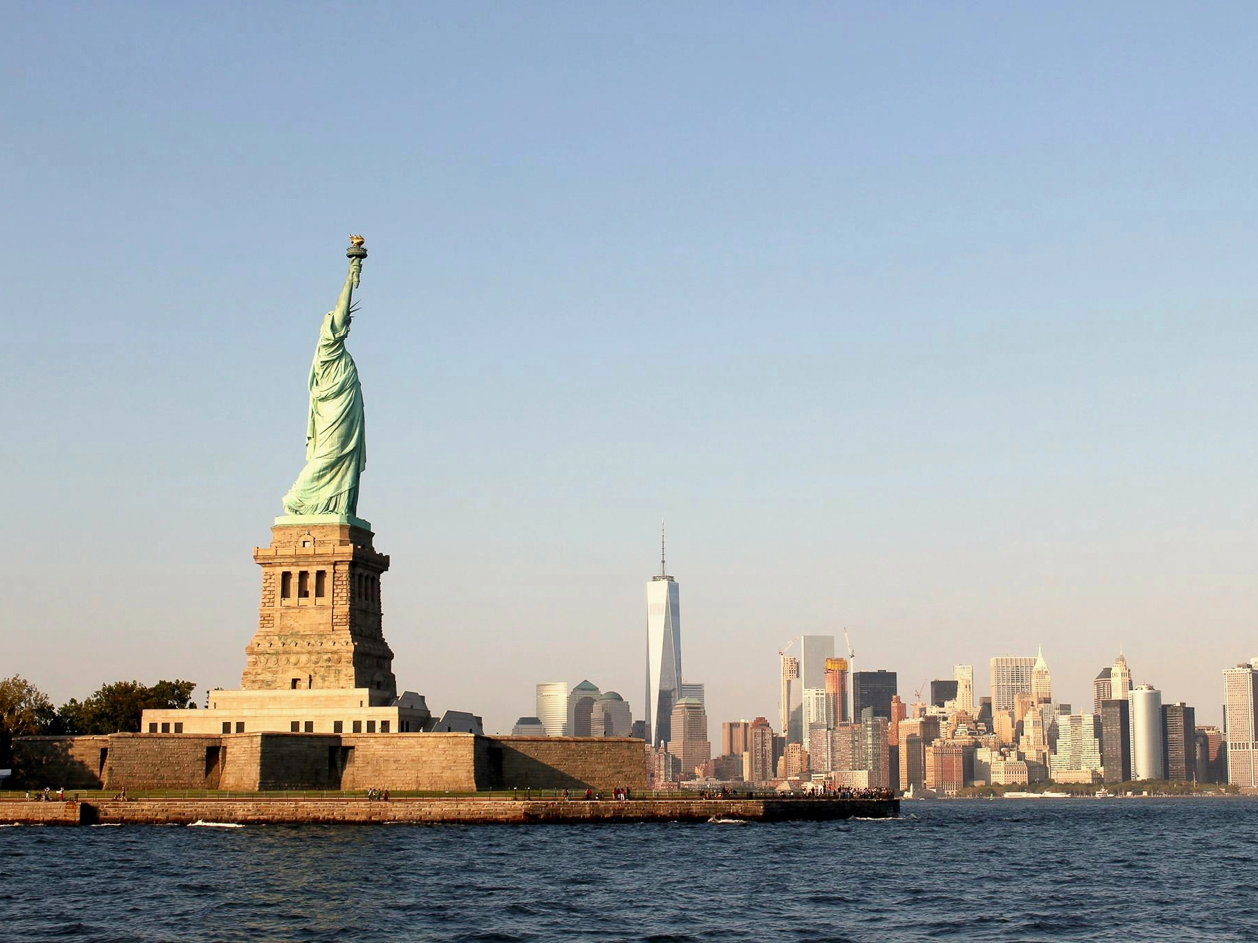 Statue of Liberty in New York Harbor with the Manhattan skyline and One World Trade Center, a major harbour city landmark.