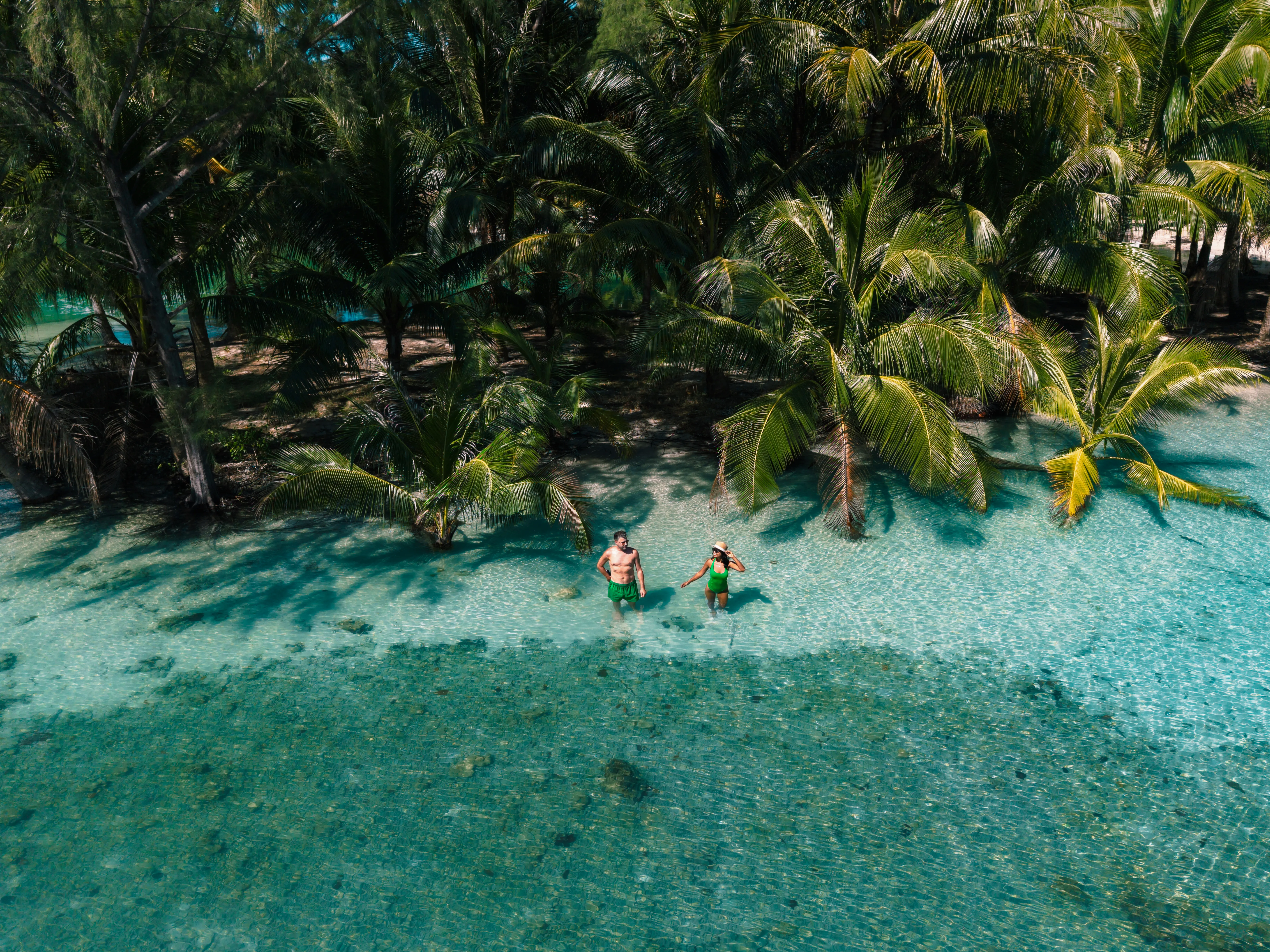 Travellers wading through a shallow turquoise lagoon surrounded by palm trees at a tropical island destination in Thailand.