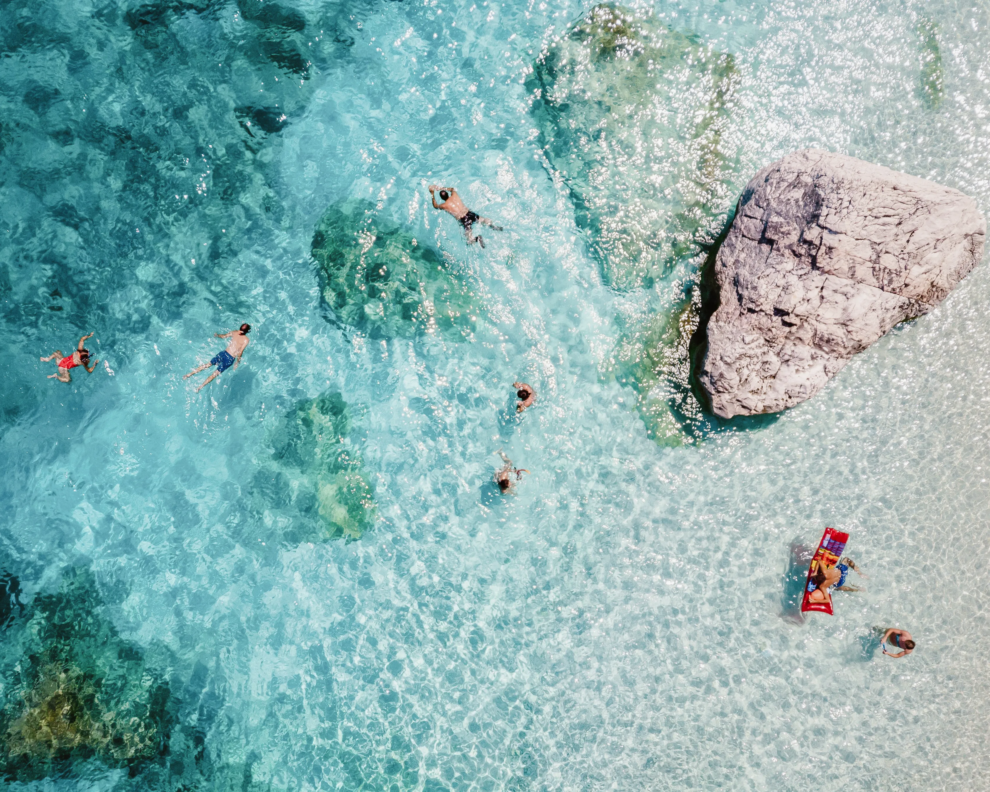 Aerial view of families swimming in clear turquoise water at a beach destination popular with kids