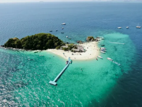 Aerial view of a tropical Thai beach with calm water and palm trees on an island.