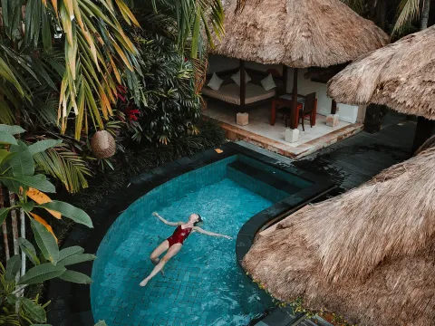 Private pool villas with thatched roofs at a tropical resort in Bali, Indonesia, surrounded by greenery