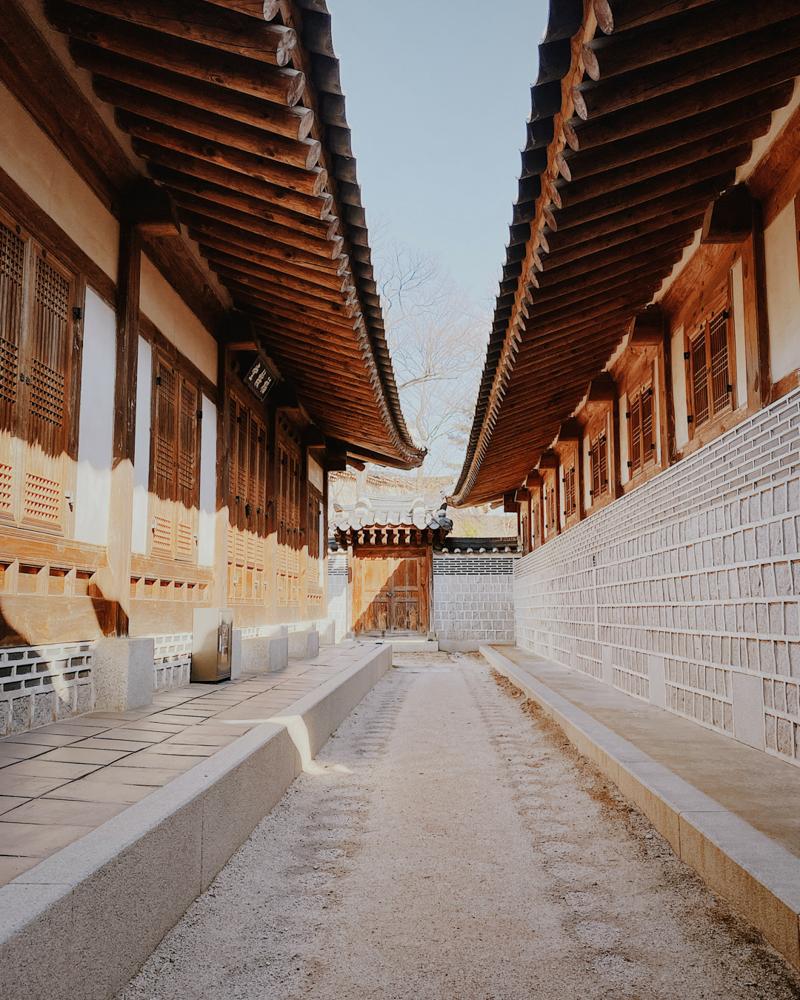 Narrow stone alleyway lined with traditional hanok houses in a historic Korean village, featuring wooden doors and tiled roofs