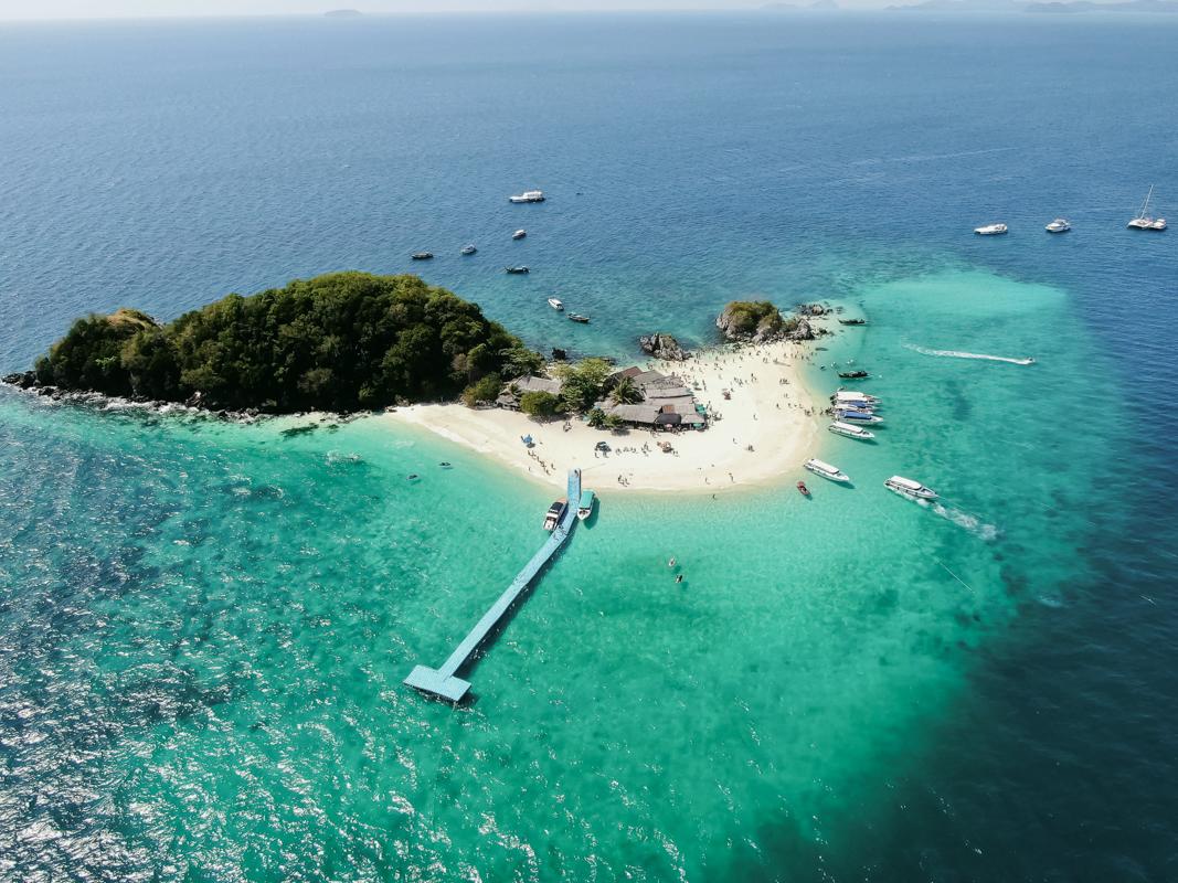 Aerial view of a tropical Thai beach with calm water and palm trees on an island.