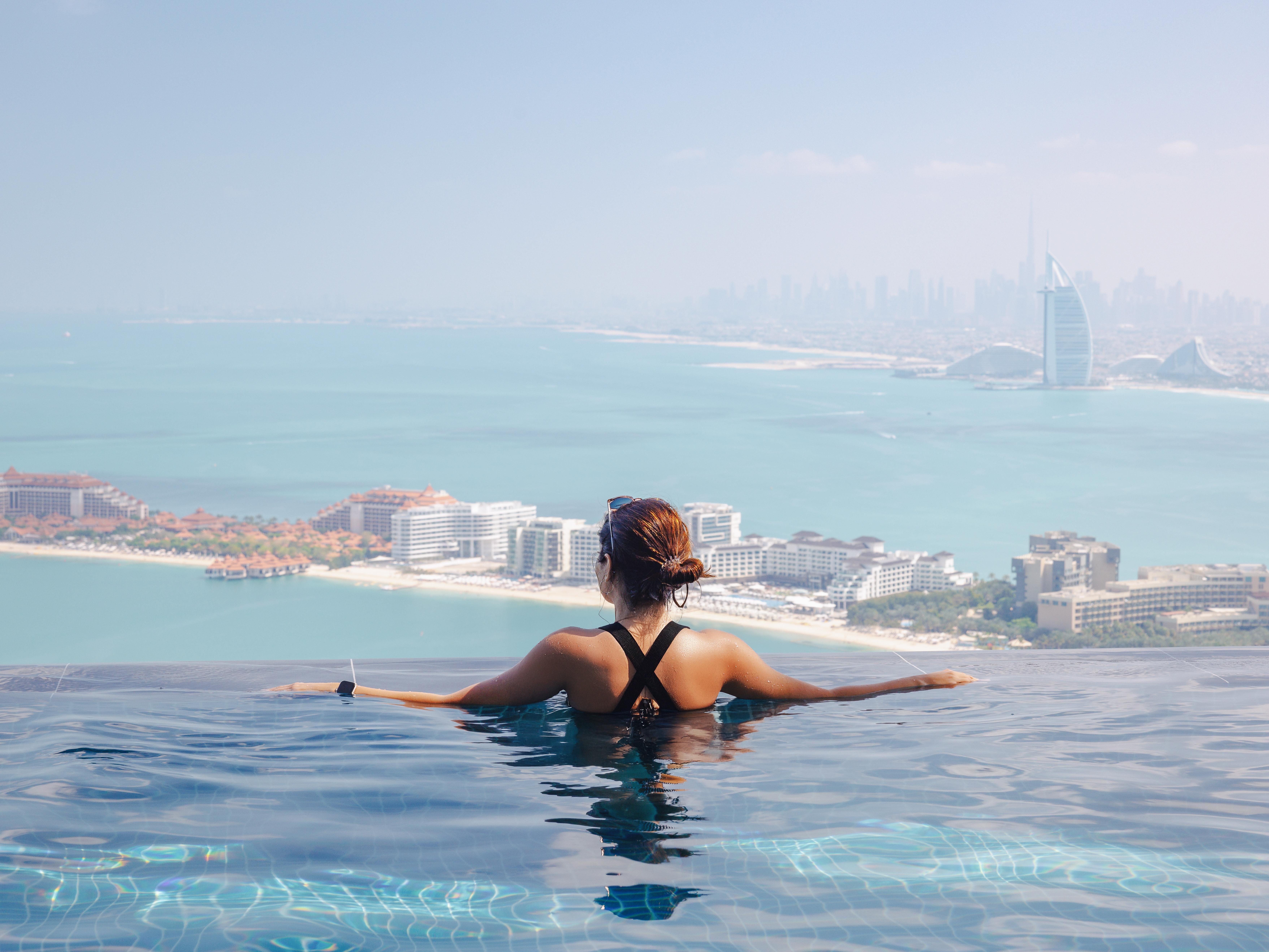 Woman relaxing in an infinity pool overlooking Dubai skyline, reflecting luxury hotels and licensed venues serving alcohol